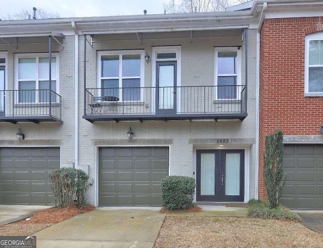 view of front of home featuring a balcony, an attached garage, driveway, french doors, and brick siding