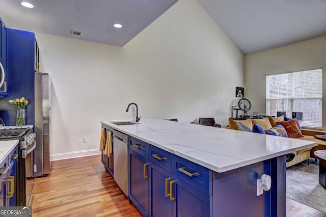 kitchen with a sink, stainless steel appliances, light wood finished floors, blue cabinetry, and light stone countertops