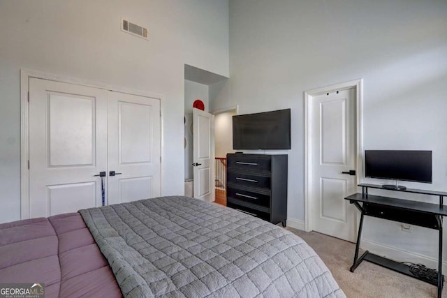 bedroom featuring a high ceiling, visible vents, light carpet, a closet, and baseboards