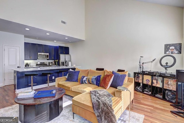 living area featuring recessed lighting, a high ceiling, visible vents, and light wood-style flooring
