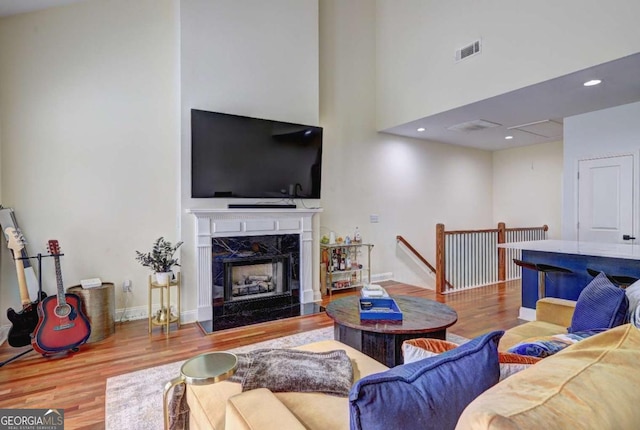 living room featuring recessed lighting, a high ceiling, wood finished floors, visible vents, and a premium fireplace