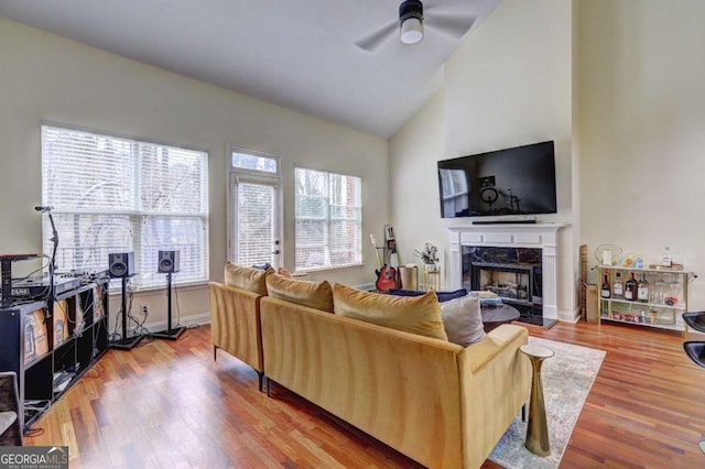 living area featuring a premium fireplace, a ceiling fan, wood finished floors, and high vaulted ceiling