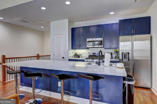kitchen with a kitchen bar, wood finished floors, visible vents, and appliances with stainless steel finishes
