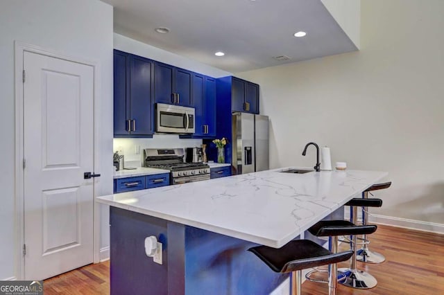 kitchen featuring stainless steel appliances, light wood-style flooring, a sink, blue cabinetry, and a breakfast bar