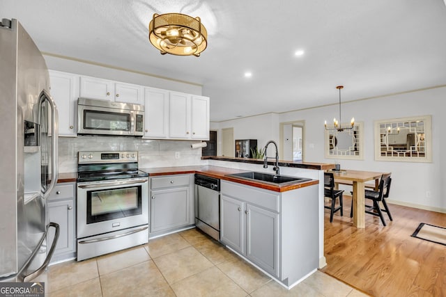 kitchen with a sink, decorative backsplash, stainless steel appliances, a peninsula, and a notable chandelier