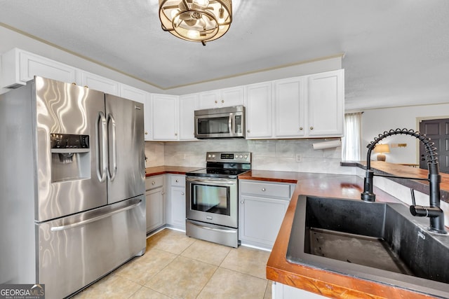kitchen with white cabinets, a sink, light tile patterned floors, decorative backsplash, and appliances with stainless steel finishes