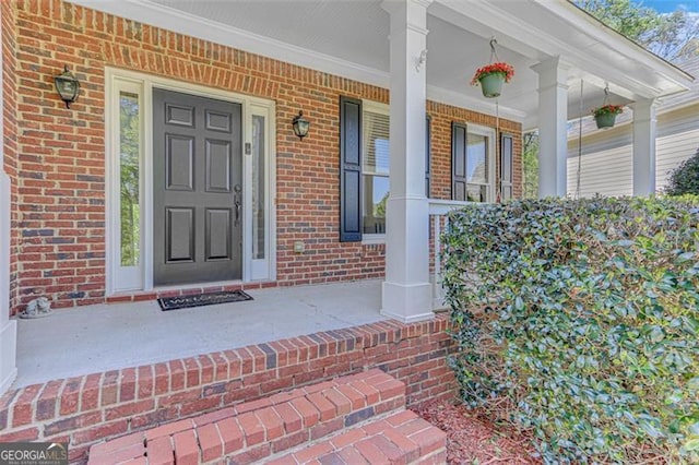 doorway to property with a porch and brick siding