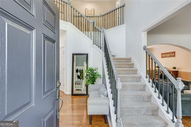 interior space featuring stairs, a high ceiling, arched walkways, and light wood-style floors