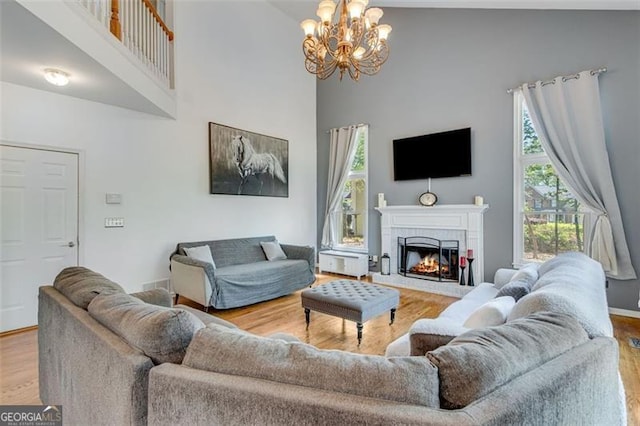 living area with an inviting chandelier, a brick fireplace, wood finished floors, and a high ceiling