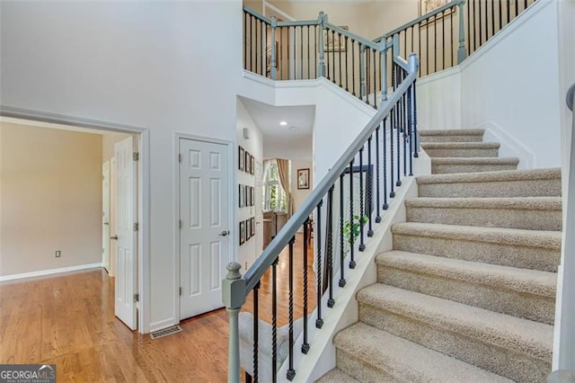 stairway with a high ceiling, wood finished floors, visible vents, and baseboards