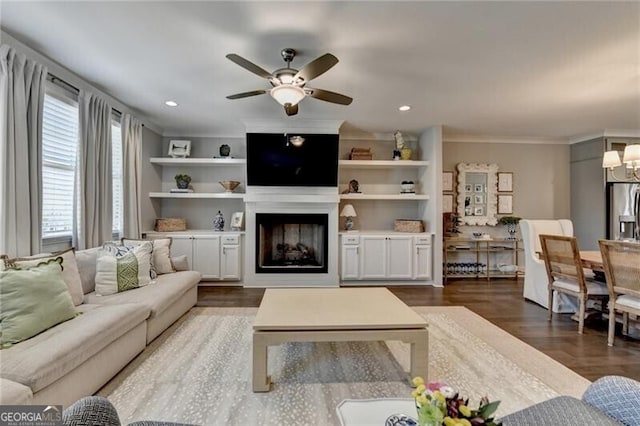 living room with ceiling fan with notable chandelier, wood finished floors, a fireplace, and ornamental molding