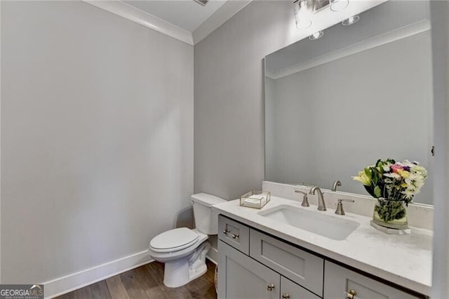 bathroom with wood finished floors, toilet, vanity, ornamental molding, and baseboards