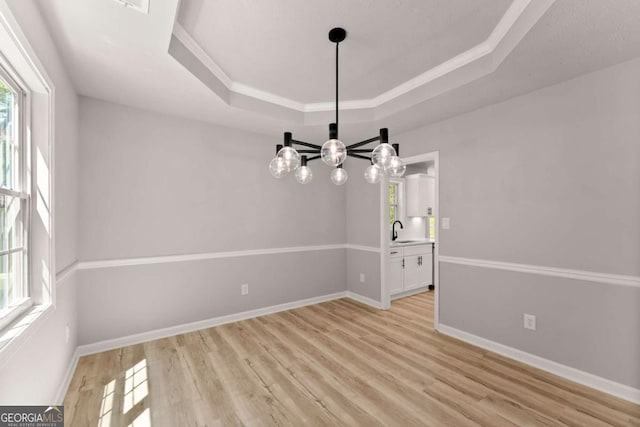 unfurnished dining area featuring a sink, baseboards, a notable chandelier, light wood-style floors, and a raised ceiling