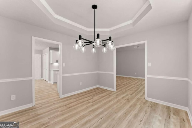unfurnished dining area with light wood-style flooring, baseboards, a notable chandelier, and a raised ceiling