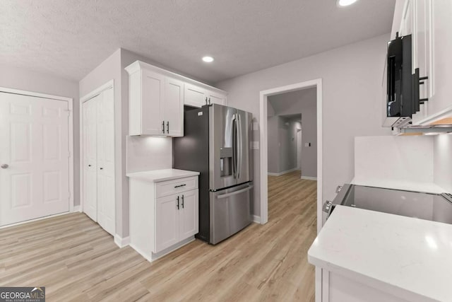 kitchen with white cabinets, light countertops, light wood-type flooring, baseboards, and stainless steel fridge