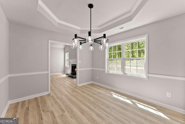 unfurnished dining area featuring light wood-style floors, an inviting chandelier, a tray ceiling, baseboards, and visible vents