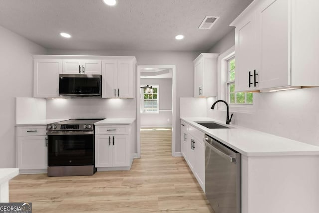 kitchen with a textured ceiling, a sink, stainless steel appliances, light wood-style flooring, and white cabinets