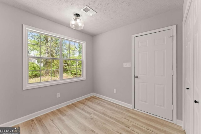 unfurnished room featuring a textured ceiling, visible vents, light wood finished floors, and baseboards