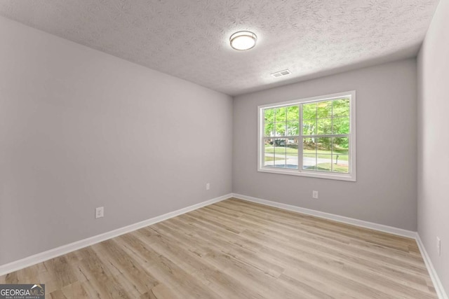 spare room featuring a textured ceiling, visible vents, light wood finished floors, and baseboards
