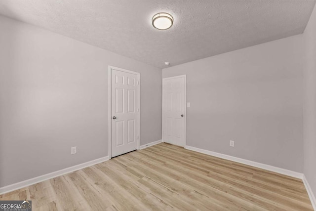 empty room with light wood-type flooring, baseboards, and a textured ceiling