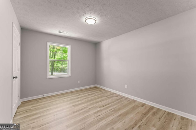 unfurnished room with light wood-style floors, baseboards, visible vents, and a textured ceiling