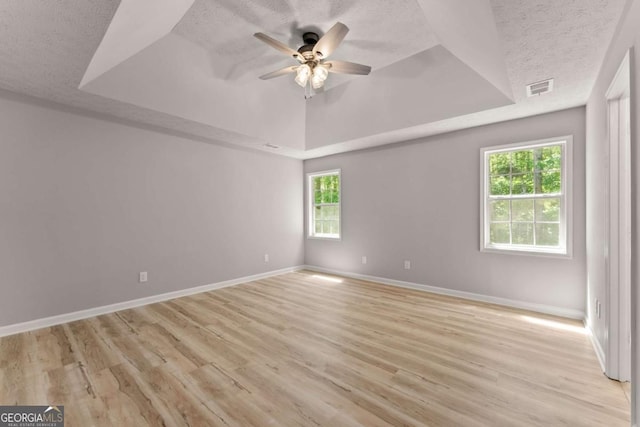 spare room with baseboards, a ceiling fan, a tray ceiling, and visible vents