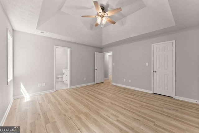 unfurnished bedroom with light wood-style flooring, visible vents, ensuite bathroom, and a raised ceiling