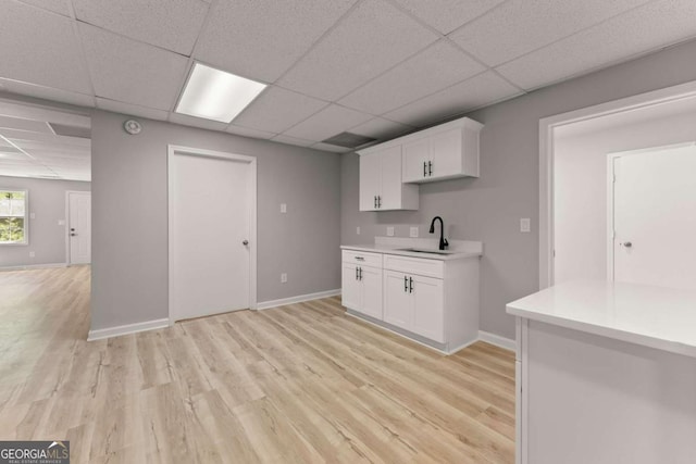 kitchen with white cabinets, light countertops, a sink, light wood-type flooring, and a paneled ceiling