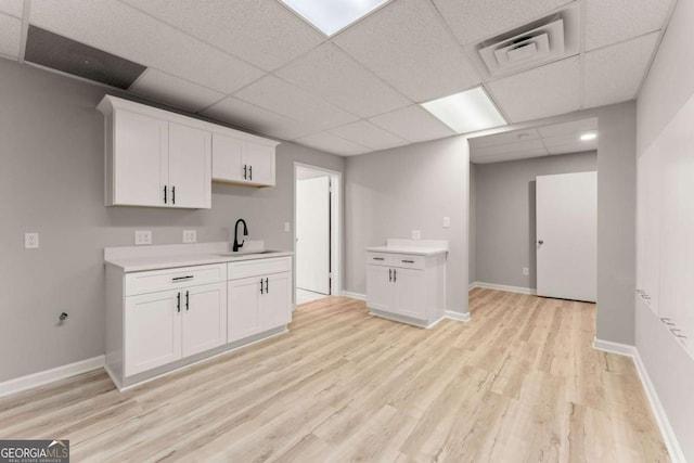 kitchen featuring white cabinets, light wood finished floors, light countertops, a sink, and a paneled ceiling