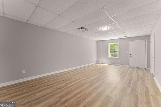 unfurnished living room featuring light wood-type flooring, visible vents, a drop ceiling, and baseboards