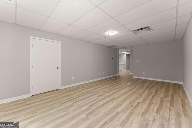 finished basement with light wood finished floors, a paneled ceiling, baseboards, and visible vents