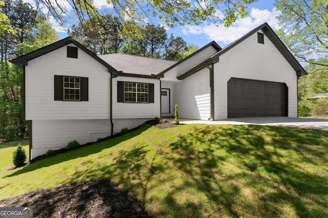 ranch-style house featuring concrete driveway, roof with shingles, a front yard, and a garage