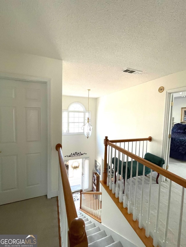 staircase with a textured ceiling, visible vents, and carpet