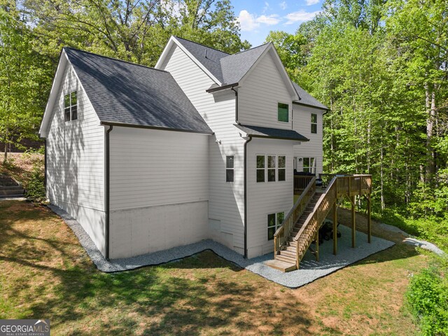 rear view of property with a wooden deck, stairway, a yard, and roof with shingles