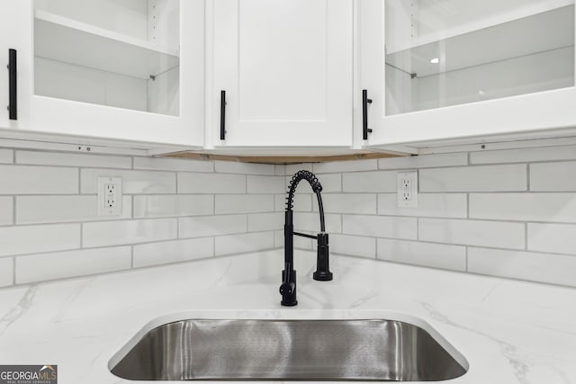 details featuring white cabinets, a sink, glass insert cabinets, light stone countertops, and tasteful backsplash