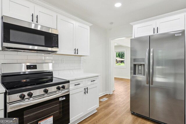 kitchen with white cabinets, stainless steel appliances, light wood-style flooring, visible vents, and backsplash