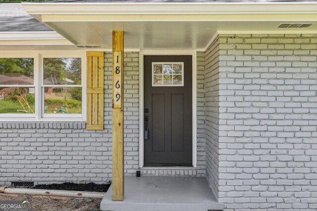 property entrance featuring brick siding and visible vents
