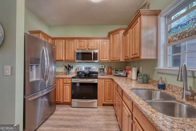kitchen with light stone countertops, stainless steel appliances, a sink, and light wood-style floors