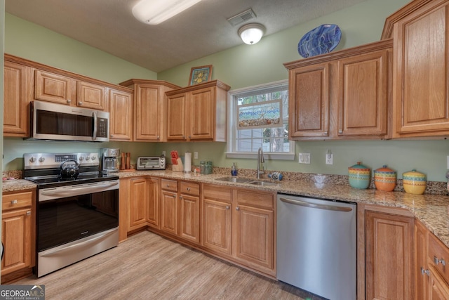 kitchen with a sink, light wood-type flooring, visible vents, light stone countertops, and appliances with stainless steel finishes