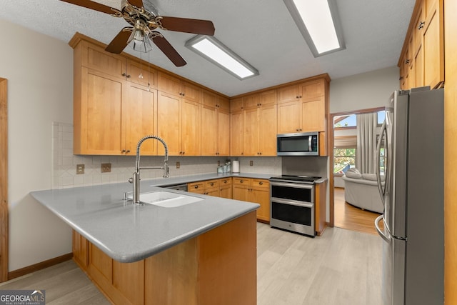 kitchen featuring stainless steel appliances, a peninsula, a sink, and light wood-style flooring
