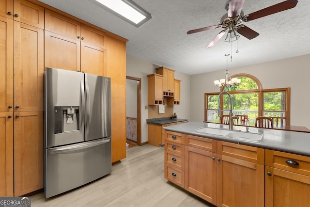 kitchen with a sink, light wood-type flooring, a textured ceiling, stainless steel refrigerator with ice dispenser, and ceiling fan with notable chandelier