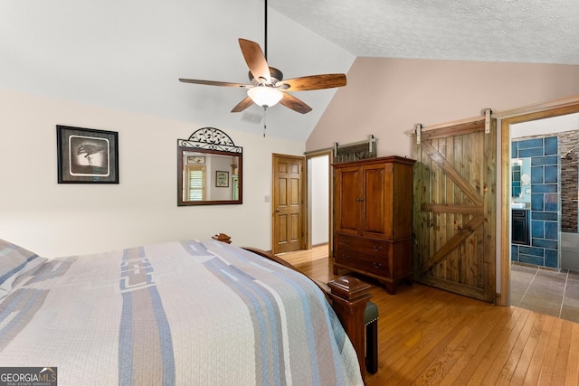 bedroom with a barn door, light wood-type flooring, visible vents, lofted ceiling, and a ceiling fan