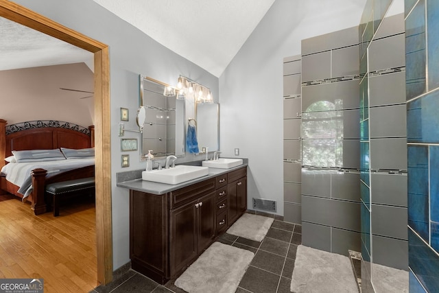 ensuite bathroom with ensuite bath, lofted ceiling, a sink, and visible vents
