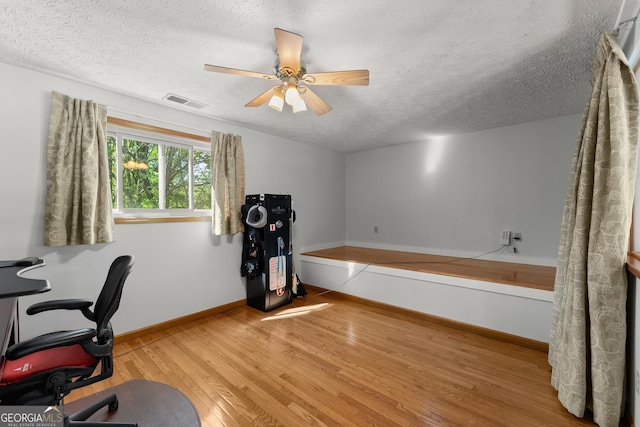 office featuring wood finished floors, a textured ceiling, ceiling fan, baseboards, and visible vents