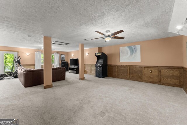 unfurnished living room featuring a textured ceiling, carpet flooring, a ceiling fan, and wainscoting