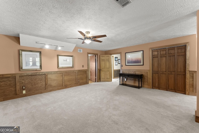 interior space featuring a textured ceiling, carpet, visible vents, and wainscoting