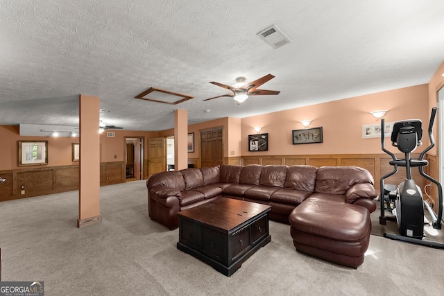 living area featuring a textured ceiling, ceiling fan, a wainscoted wall, light colored carpet, and visible vents