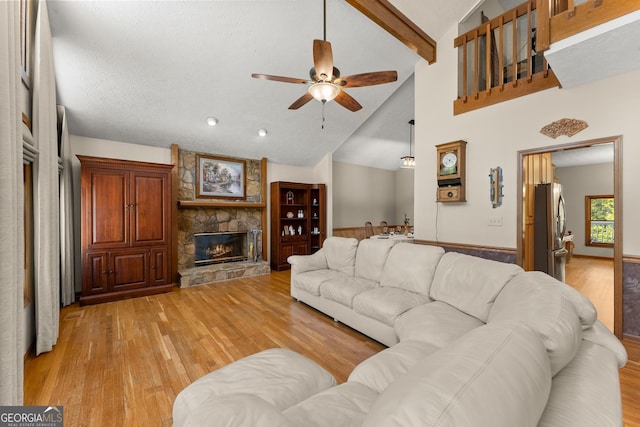 living area featuring a stone fireplace, light wood-style floors, and ceiling fan