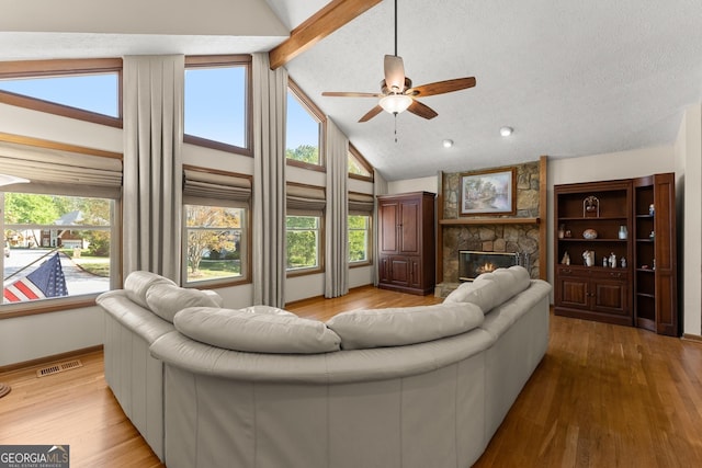 living room with a ceiling fan, visible vents, a stone fireplace, and a healthy amount of sunlight
