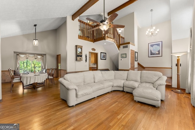 living area with high vaulted ceiling, stairs, ceiling fan with notable chandelier, light wood-type flooring, and beam ceiling